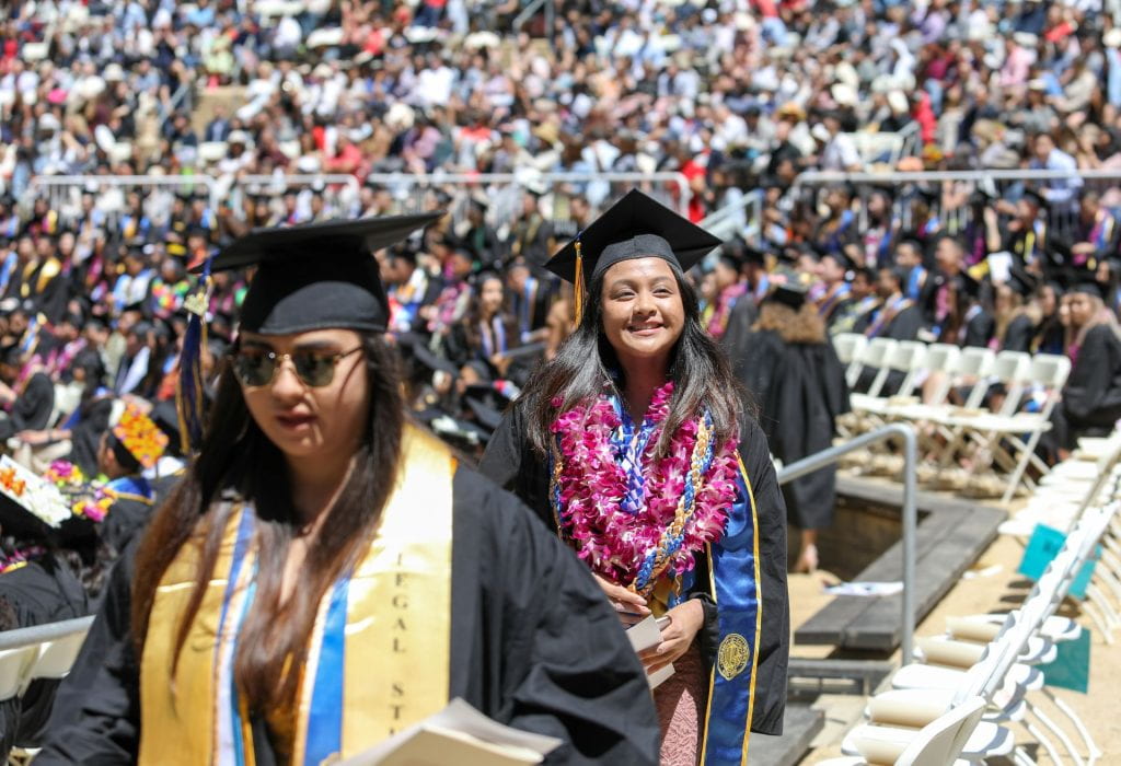 Photo of two female students at graduation, walking and smiling.  