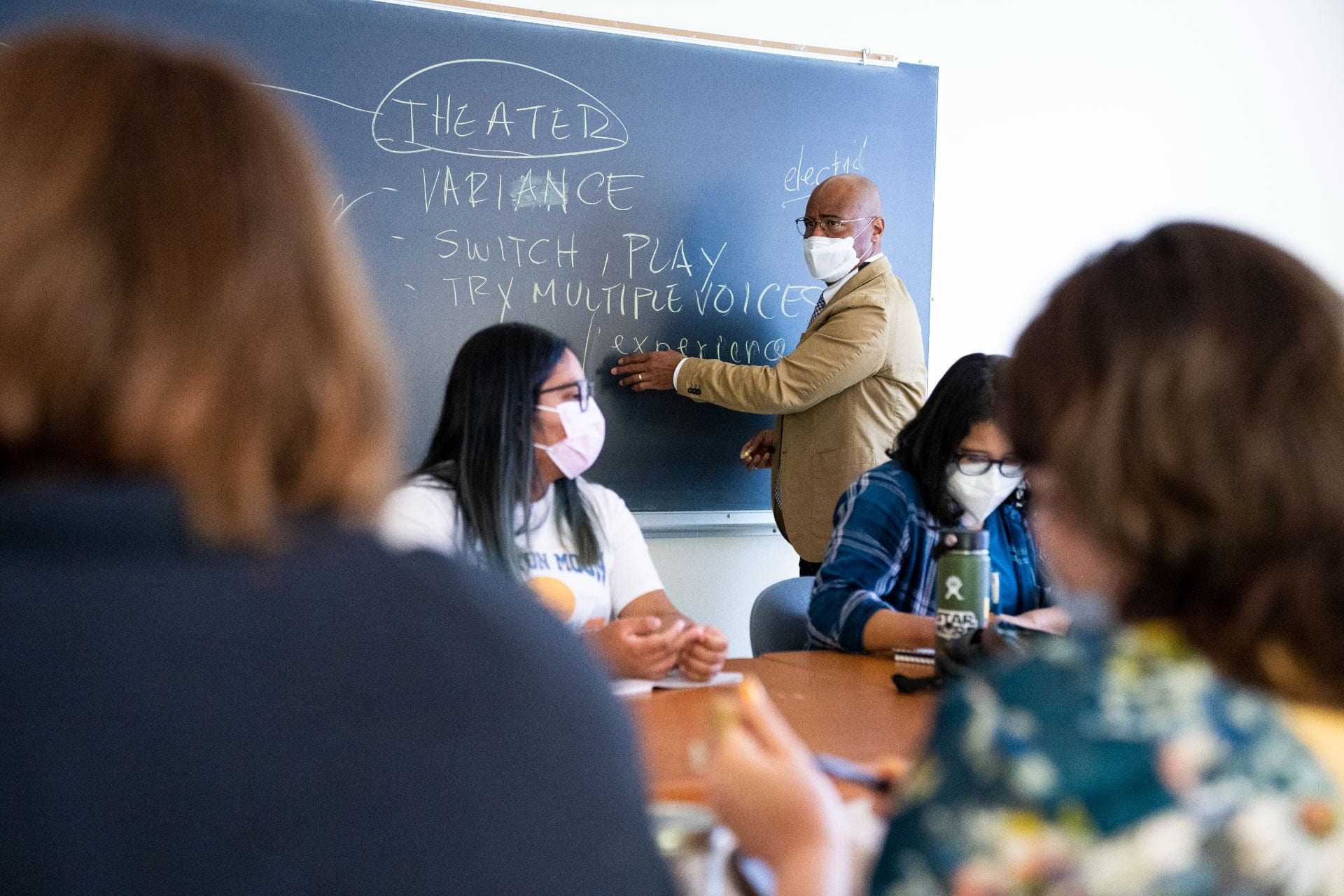 Photo of faculty member facing chalk board with four students at large table.  